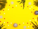 Яркий желтый фон с зелеными еловыми ветками, серебристыми шариками и снежинками, красными и белыми звездами по краям